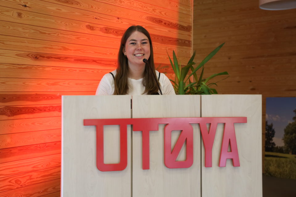 Leder av AUF Astrid Willa Hoem har et stort smil og står på en talerstol med skriften Utøya